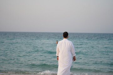 Middle Eastern way dressed Arab man standing in front of a beach.