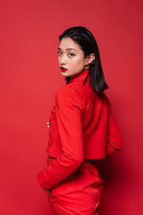 Fototapeta premium asian woman in stylish clothes standing with hand in pocket and looking at camera on red background.