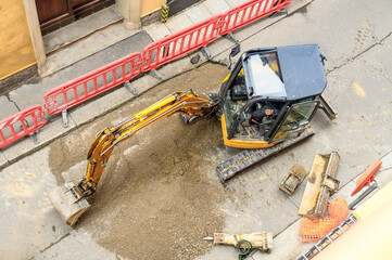 Top view of a small excavator in the process of roadworks on a narrow city street