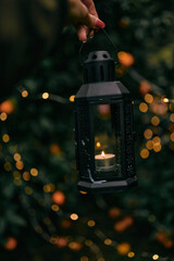 a glass lamp with candles against the backdrop of an orange orchard and Christmas lights - 552105771