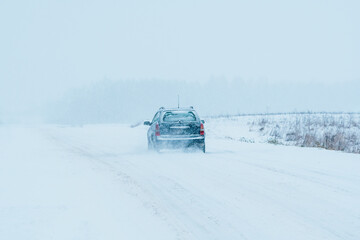 The car is driving on a road in a blizzard