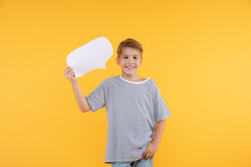 Happy smiling Caucasian boy holding blank speech bubble, empty word cloud, looking to camera against yellow background.