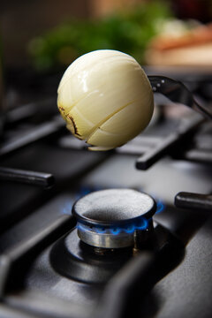 Opalanie cebulki do rosołu nad palnikiem na kuchence gazowej