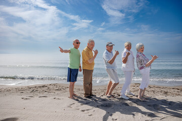 gruppo di 5 anziani al mare  giocano felici facendo il segno di "ok" con il dito