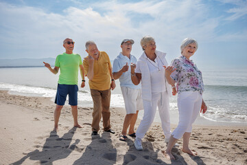 gruppo di 5 anziani al mare  giocano felici facendo il segno di 