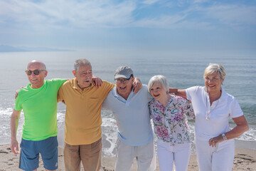 gruppo di 5 anziani al mare  si abbracciano  felici - sullo sfondo si vede il cielo blu