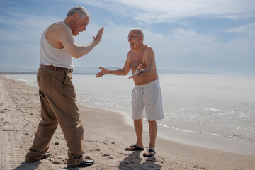 coppia di anziani al mare giocano divertiti dandosi il segno di "ok" con le mani