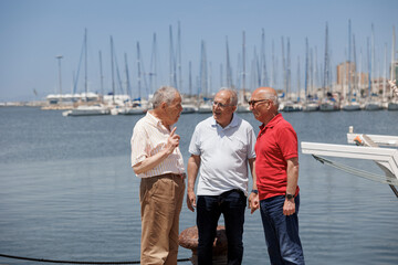 gruppo di tre anziani amici discute in piedi nei pressi di porto turistico 