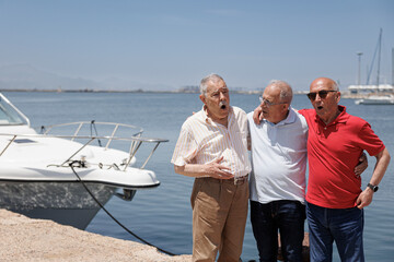 gruppo di tre anziani amici discute in piedi nei pressi di porto turistico 