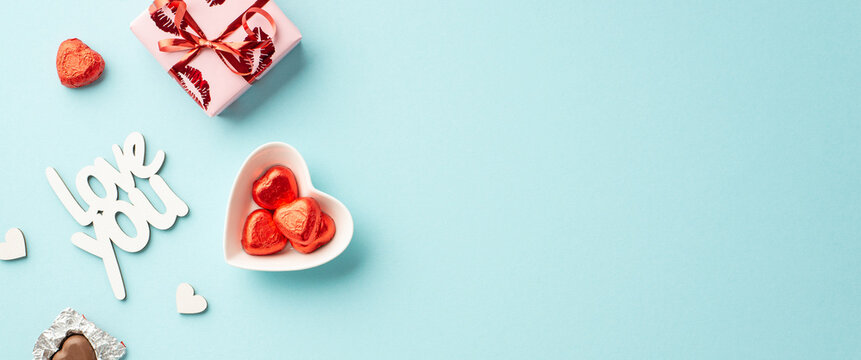 Valentine's Day concept. Top view photo of giftbox in wrapping paper with kiss lips pattern heart shaped saucer with candies and inscription love you on isolated pastel blue background with copyspace - Powered by Adobe