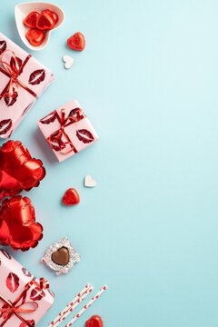 Valentine's Day concept. Top view vertical photo of gift boxes heart shaped balloons saucer with chocolate candies and straws on isolated pastel blue background with empty space