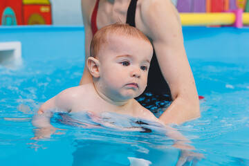 Fototapeta na wymiar A beautiful mother teaches teaches her little son how to swim in the pool. A child is having fun in the water with his mother. Child development. First swimming lessons for children