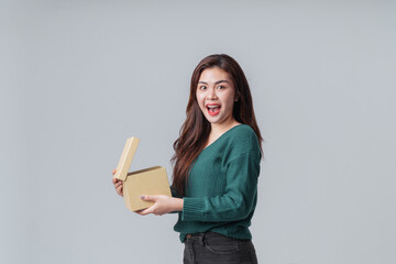 Surprise Asian woman in casual green sweater open a gift box on isolated grey background. Happy anniversary or new year festival concept.