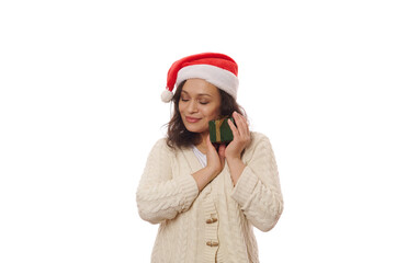 Multi-ethnic brunette wearing Santa hat and beige knitted sweater, hugging her happy present for Christmas or New Year. Boxing Day. Xmas - December 25th. Happy atmosphere of upcoming winter holidays