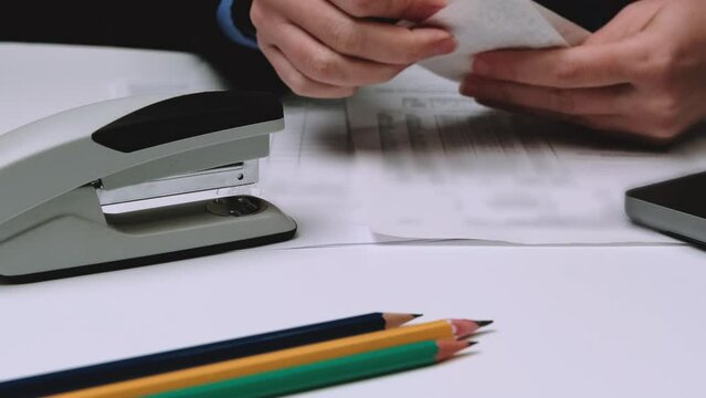a business woman holds cash receipts in her hands and staples them with a stapler.