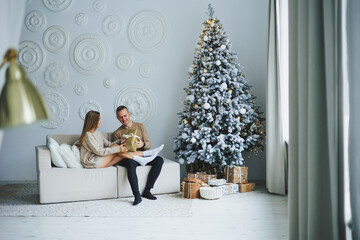 A happy couple celebrates the New Year at home near a Christmas tree decorated with toys and garlands. Lovers welcome the new year together. New Year and Christmas concept. February 14th.