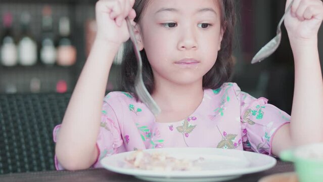 Face Close up of adorable asian girl kid who is hungrily eating macaroni with fork and spoon on table for her breakfast shows concept of delicious meal with healthy food for children.