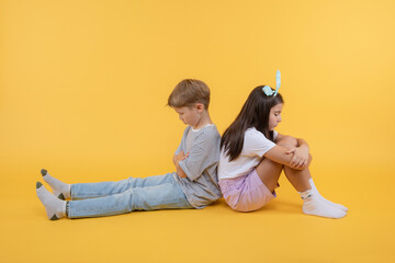 Two siblings brother and sister mad at each other. Two friends boy and girl sitting on the floor back to back, offended at each other. Teenage quarrels, difficulties of transitional age.