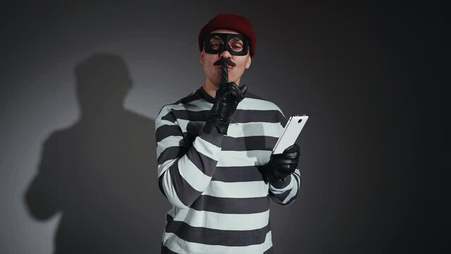 funny thief in mask and Prison Uniform with a laptop in hand finger to the lips