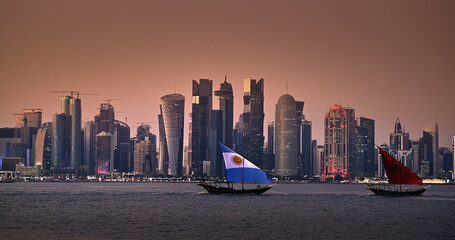 Traditional boats sail with Argentina and Morocco country flags design for FIFA World Cup 2022 in Corniche area with amazing sunset view of cityscape skyscraper buildings in Doha, Qatar