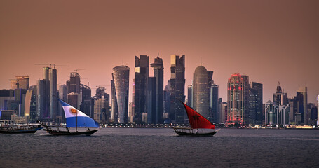 Traditional boats sail with Argentina and Morocco country flags design for FIFA World Cup 2022 in Corniche area with amazing sunset view of cityscape skyscraper buildings in Doha, Qatar