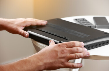 Repairman's hands removing the power battery from the laptop. Computer service and repair concept. Laptop disassembling in repair shop. Electronic development, electronic device fixing.