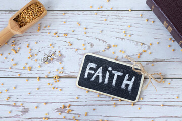 Faith handwritten text word with chalk, spoon with mustard seeds, and closed holy Bible book on...