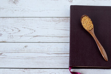 Spoon with mustard seeds on top of holy Bible Book placed on wooden background with copy space. Top...