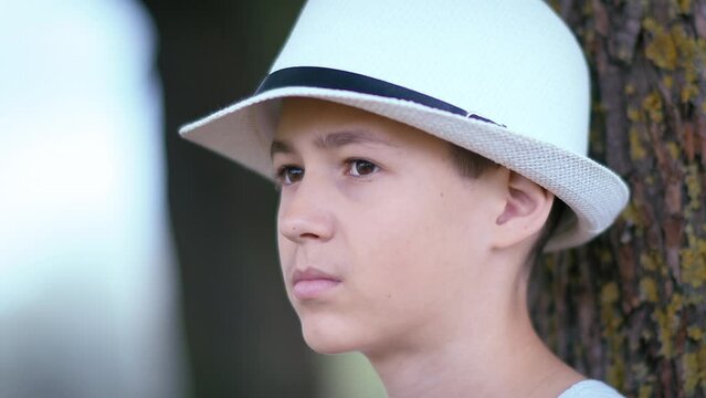 portrait of a boy angrily looks at people passing by in the park, portrait of a boy sitting under a tree in the park, malevolent boy