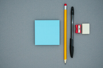 Pencil, pen, scraper, eraser and blue blank sticky notes, on a gray background, top view. School office supplies