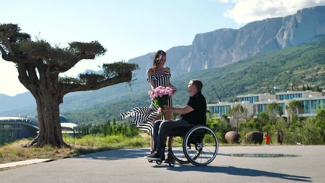 Man in a chair for people with physical disabilities gives a bouquet of flowers to his bride.