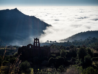 imagen valle de monta&ntilde;as con una iglesia en contraluz en lo alto de una monta&ntilde;a y nubes al fondo