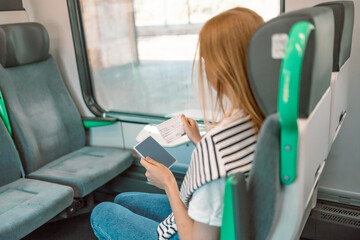  Caucasian blonde woman sitting in the high-speed train holds in her hand ticket and passport for the train traveling from the airport to the city while traveling by Krakow, Poland 