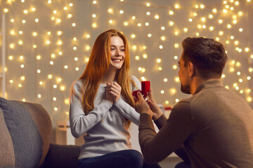 Will you marry me. Man in love kneels in front of a girl with a wedding ring in his hands and offers her marriage. Man holds a red box with a wedding ring in front of his beloved.