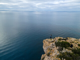 Person on cliff standing looking towards the horizon.