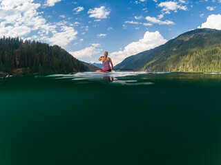 Adventurous athletic woman sitting on a paddle board on a large alpine lake in the Pacific Northwest on a beautiful summer day.
