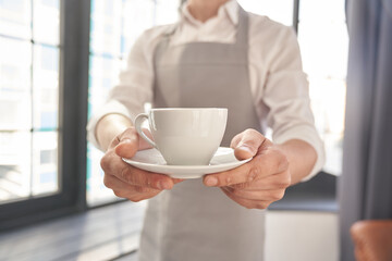 Your coffee, please. Cropped image of a man holding a cup of good coffee against the background of a window. With space to copy. High quality photo