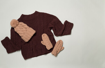 Sweater and winter hat with mittens on color background, top view