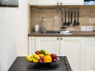 Close-up of fresh fruits on plate. Blurred kicthen in background. Sink, black spoons on wall.