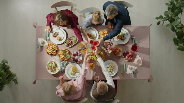 Top down shot of family clinking glasses in toast and then drinking while having festive dinner on Easter day