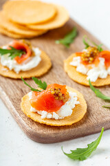 Small finger food salmon and cream cheese appetizers served on wooden board, close up