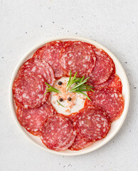 Round plate with thin slices of salami decorated with pepper and rosemary