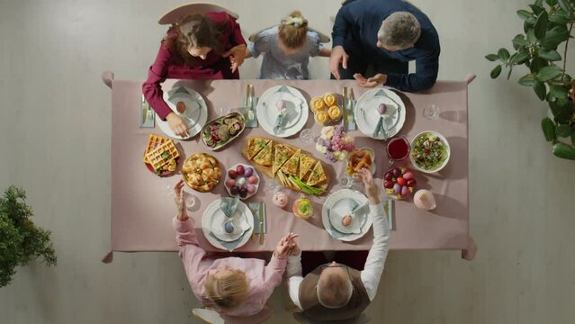 Top down shot of family holding hands and praying before having holiday meal at dinner table on Easter day