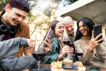 Young friends having fun drinking red wine at winery bar outdoors- Happy cheerful people looking smartphone sharing social content on mobile phone together at restaurant-Youth Lifestyle Concept