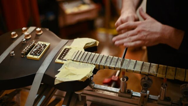Luthier hands polishing the frets on the fretboard of the black electric guitar