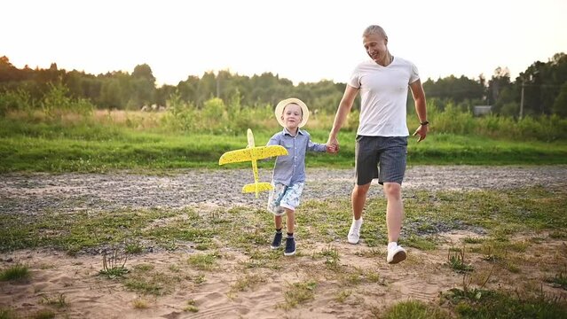 Happy father and son run with airplane model outdoors at sunset. The concept of rest, imagination, holidays, freedom. Father and son spending time together. High quality FullHD footage