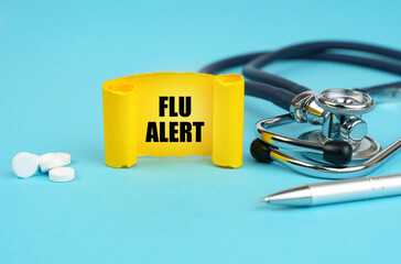 On a blue surface, a stethoscope, pills, a pen and a yellow sign with the inscription - Flu alert