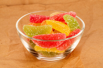 Several sweet marmalade candies in a glass plate on kraft paper, macro.