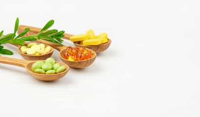 Herbs, capsules and pills in wooden spoons on white wooden background. Herbal medicine concept