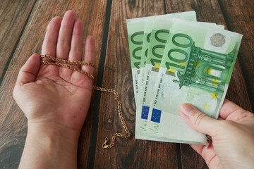 One hand hold golden chain and other hand hold stack of euro money on  wooden background, pawnshop © lesslemon